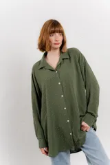 Camisa verde militar con estampado de lunares blancos, de corte oversize, con cuello camisero, cierre frontal con botones y bolsillo en el pecho.