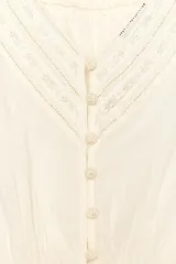 Blusa color crudo de cuello redondo y manga corta con puños. Presenta bordados a tono y cierre trasero con botones forrados.