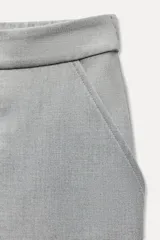 Pantalón tobillero negro de tiro medio con cintura elástica en la espalda, bolsillos delanteros y bolsillos de parche con solapa en la parte trasera. Bajo acabado con pinzas. Cierre frontal con cremallera y botón.