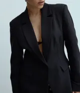 Blazer femenino estructurado de poliéster color negro, con modelo alargado, cuello solapa, cierre frontal con un único botón y bolsillos delanteros.
