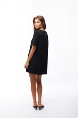 Vestido corto negro de poliéster y elastano, con cuello redondo y mangas cortas. Presenta dos bolsillos frontales con botón dorado.