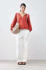 Remera color ladrillo con bordados blancos en el escote y mangas largas con puños elásticos.