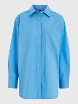 Camisa celeste de popelín de algodón orgánico, corte oversize con hombros caídos, cuello inglés, bolsillo de parche en el pecho y logo bordado en la manga.