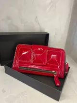 Billetera tipo clutch de cuero charol color rojo, con cierre de cremallera y broche imantado. Diseño con compartimentos internos y ranuras para tarjetas.
