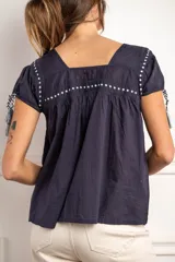 Blusa de algodón color blanco con bordado negro y mangas cortas, detalles de tirantes con borlas.