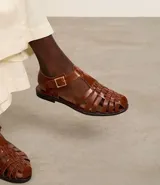 Sandalias planas de cuero marrón con tiras entretejidas, hebilla dorada y suela negra.