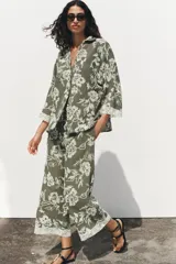 Camisa verde militar con bordado floral blanco, cuello solapa, escote en pico, manga tres cuartos con detalle de guipur y cierre frontal con botones.