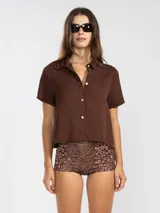 Camisa marrón de manga corta confeccionada en lino tencel. Presenta cuello camisero y cierre frontal abotonado.