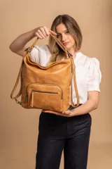 Cartera mochila color tostado, símil cuero, con compartimiento principal amplio y bolsillos frontales con cierre. Tiene correas ajustables para usar como mochila y asa superior para llevar al hombro.