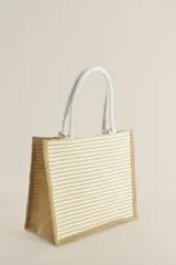 Bolso tipo tote de yute con rayas horizontales color beige y manijas de soga blanca.