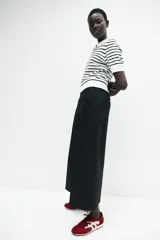 Pantalón palazzo negro de tiro alto con elástico oculto en la cintura, cierre lateral oculto y pinzas que realzan la figura. Modelo de corte holgado con bolsillos al bies, bolsillos decorativos atrás y piernas tres cuartos con raya adelante y atrás.