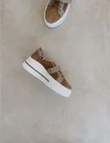 Zapatillas deportivas urbanas con capellada negra, detalles en beige y suela blanca.