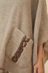 Poncho de lana color marrón con cuello alto, mangas 3/4 y bolsillo lateral con detalle de botones de cuero.