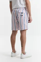 Short de baño largo a rayas verticales en tonos rosa, azul y blanco. Tiene cintura elástica con cordón ajustable, dos bolsillos laterales y uno trasero.