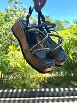 Sandalias negras con tiras entrecruzadas y suela plana, diseñadas para brindar comodidad y seguridad.