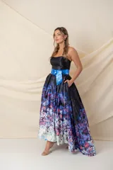 Vestido largo strapless con corpiño negro y falda estampada con degradé floral en tonos azules, violetas y blancos. Falda amplia con tablas y bolsillos, armada con tul y más larga atrás. Incluye cinturón azul con hebilla circular. Modelo único.