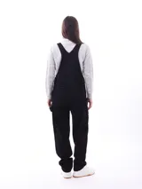 Mono enterizo negro de corte holgado con tirantes regulables y bolsillos laterales. Presenta un bolsillo tipo parche en el frente.