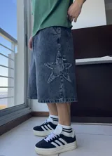Bermuda de jean gris oscuro, corte ancho y largo a la rodilla, con diseño de estrella rota en el muslo.