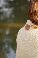 Poncho tejido en lana merino color crudo, con cuello alto y etiqueta de cuero con logo en la espalda.