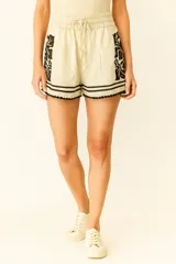 Short de viscosa color crema, con cintura elastizada y cordón ajustable. Presenta bordados florales negros en los laterales y terminación con puntilla negra en el ruedo.