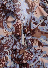 Blusa de gasa estampada con motivos paisley en tonos marrón, celeste y rosa. Tiene escote en V con volantes, mangas largas con puños elásticos y corte holgado.