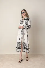 Vestido camisero midi de lino y viscosa color crudo con estampado de palmeras en negro. Tiene cuello camisero, mangas largas con puños y cinturón de la misma tela.