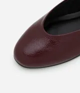 Zapatilla color borgoña de charol sintético, con puntera redonda, tira sobre el empeine con hebilla metálica plateada y taco bajo.