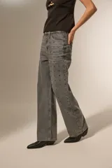 Pantalón gris de denim con corte recto, tiro alto y apliques de tachas cuadradas plateadas en los laterales.