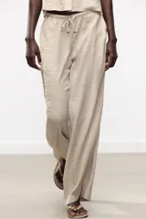 Pantalón de tiro alto color beige, con cintura elástica ajustable con cordones, bolsillos delanteros y pernera ancha.