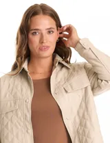 Chaqueta tipo camisa (shacket) de eco cuero color beige, con diseño acolchado en rombos, cuello camisero, botones frontales y dos bolsillos de parche en el pecho.