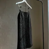 Vestido corto negro con estampado de líneas onduladas plateadas y tirantes de cadena metálica.