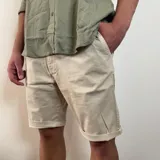 Bermuda color beige claro, estilo chino, confeccionada en gabardina. Presenta un corte recto y dobladillo en el ruedo.