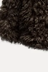 Abrigo corto de pelo sintético color marrón, con cuello solapa y manga larga. Tiene bolsillos delanteros, forro interior y cierre frontal con ganchos metálicos forrados.