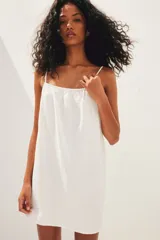 Vestido corto blanco de muselina de algodón suave, corte holgado, con breteles finos ajustables, escote recto y espalda redondeada.