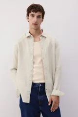 Camisa de lino color crema, de corte recto, con cuello inglés, tapeta clásica, mangas largas con puños abotonados y bajo redondeado.