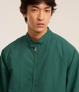 Campera bomber verde oscuro de poliéster con cuello alto con velcro, cierre por cremallera, bolsillos con solapa, manga larga ajustada y bajo ajustado.