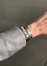 Pulsera rígida plateada, con diseño de banda ancha y detalles de apliques redondos blancos y perforaciones.