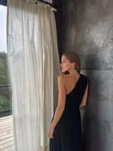 Vestido largo negro de un solo hombro, confeccionado en tela tableada con sutiles brillos.