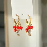 Aros dorados tipo argolla con dijes colgantes de cuentas rojas y cristal facetado.