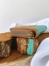 Billetera pequeña de cuero turquesa con textura de reptil y detalles en cuero marrón. Tiene cierre metálico y monedero interno.