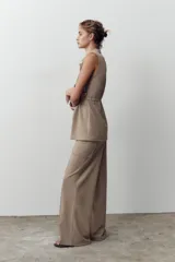 Pantalón de sarga color beige, de tiro medio con cintura elástica en la espalda, bolsillos laterales de plastrón con botón metálico y pierna ancha.