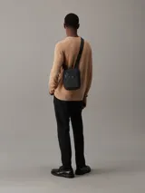 Cartera negra de poliéster reciclado con ribete de piel sintética y correa ajustable para usar como cartera o riñonera.