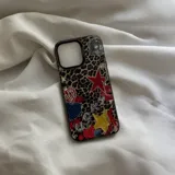 Funda protectora para celular con diseño de estampado de leopardo y múltiples parches decorativos, incluyendo estrellas, corazones, frutas y una bola de espejos.