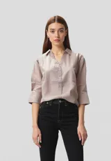 Camisa color lila claro de algodón, corte holgado, con cuello camisero, cierre frontal con botones y mangas 3/4 con puños.