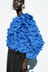 Chaqueta azul con cuello redondo y manga larga, con apliques de pétalos en toda la prenda y cierre frontal con botón a presión oculto.