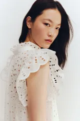 Vestido corto blanco de algodón con broderie, cuello alto con volados, mangas cortas con volados, botonadura frontal y falda con volados.