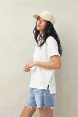 Remera blanca de manga corta confeccionada en algodón liviano con textura levemente jaspeada. Presenta tajos laterales y costura central al frente.