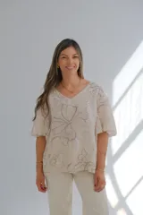 Blusa beige con estampado floral en tonos grises, escote en V y mangas cortas.