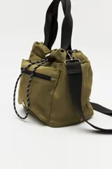 Cartera tipo bolso de nylon negro, con diseño utilitario y formato flexible que se ajusta con cordón en la parte superior. Posee asas de mano y una correa ajustable y desmontable para llevar cruzada. Incluye bolsillo frontal con cierre y herrajes metálicos.