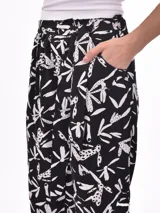 Pantalón babucha de tela estampada con hojas en tonos rosa, naranja y azul, con cintura elastizada y lazo para ajustar.
